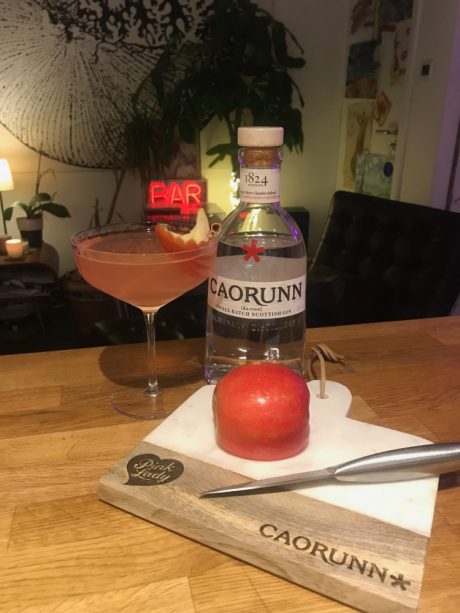 A pink cocktail drink next to a bottle of Caorunn gin.